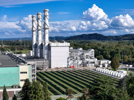Aerial view of the A2A Chivasso Power Plant featuring three tall industrial chimneys and modern facilities surrounded by green hills and trees in Chivasso Piemonte Italy. Aerial view of the A2A Chivasso Power Plant featuring three tall industrial chimneys and modern facilities surrounded by green hills and trees in Chivasso Piemonte Italy.