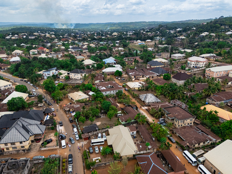Aerial view of a sprawling community with a tapestry of dark grey and light colored roofs nestled amidst vibrant green foliage crisscrossed by busy roads under an overcast sky Ohafia Abia Nigeria. Aerial view of a sprawling community with a tapestry of dark grey and light colored roofs nestled amidst vibrant green foliage crisscrossed by busy roads under an overcast sky Ohafia Abia Nigeria.