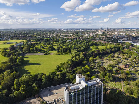 Aerial view of Gunnersbury Park featuring green lawns dense trees and a modern building in the foreground with the London skyline in the distance London England United Kingdom. Aerial view of Gunnersbury Park featuring green lawns dense trees and a modern building in the foreground with the London skyline in the distance London England United Kingdom.