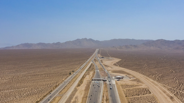 Aerial view of a highway stretching through a vast arid desert landscape with mountains in the background United States.