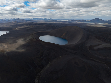 Aerial view of a volcanic crater lake surrounded by dark basaltic lava fields under a cloudy sky in Iceland. Aerial view of a volcanic crater lake surrounded by dark basaltic lava fields under a cloudy sky in Iceland.
