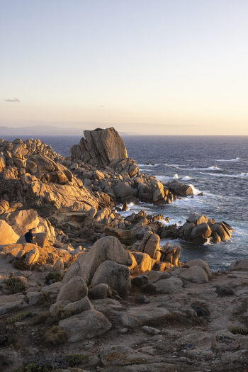 View of the granite rock formations and rugged coastline with a person sitting on the boulders at sunset Capo Testa Sardegna Italy.