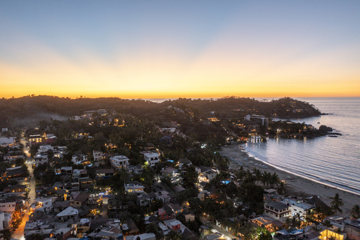 Aerial view of the coastal town of Sayulita at sunset featuring illuminated buildings lush hills and the Pacific Ocean coastline in Sayulita Nayarit Mexico. Aerial view of the coastal town of Sayulita at sunset featuring illuminated buildings lush hills and the Pacific Ocean coastline in Sayulita Nayarit Mexico.