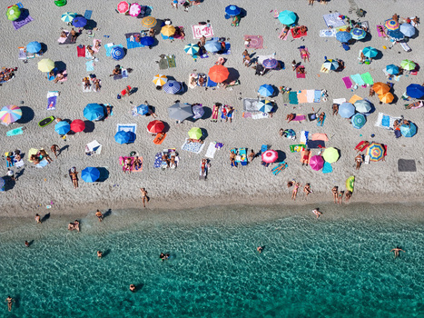 Aerial view of a crowded public beach with colorful umbrellas and people relaxing on the sand by the clear turquoise water in Bergeggi Liguria Italy.