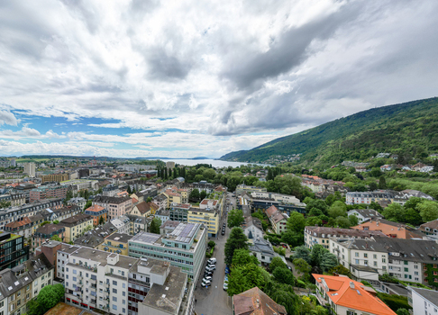 Aerial view of the urban landscape featuring residential buildings lush green trees and the scenic Lake Biel under a dramatic cloudy sky Biel Bienne Canton of Bern Switzerland. Aerial view of the urban landscape featuring residential buildings lush green trees and the scenic Lake Biel under a dramatic cloudy sky Biel Bienne Canton of Bern Switzerland.
