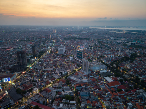 Surabaya Indonesia 28 August 2026 Aerial view of the urban landscape of Surabaya at sunset with dense residential rooftops high rise buildings and glowing city lights.