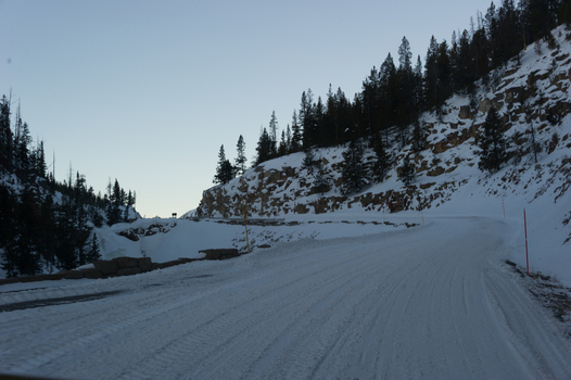 View of a snow covered road winding through the winter landscape of Yellowstone National Park with pine trees and rocky cliffs Yellowstone National Park Wyoming United States. View of a snow covered road winding through the winter landscape of Yellowstone National Park with pine trees and rocky cliffs Yellowstone National Park Wyoming United States.
