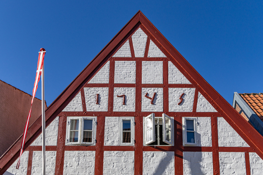 View of a traditional half timbered house gable with red beams and white brickwork under a clear blue sky in Ribe Denmark. View of a traditional half timbered house gable with red beams and white brickwork under a clear blue sky in Ribe Denmark.