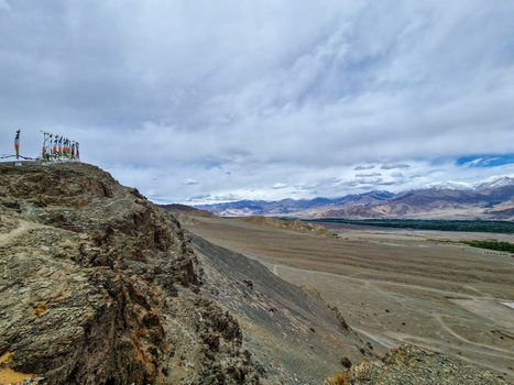 View of Matho Gompa with prayer flags on a rocky ridge overlooking the arid landscape and distant snow capped mountains Matho Ladakh India.
