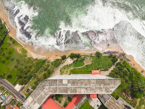 Aerial view of a modern building and powerful waves crashing against the sandy coastline in Galle Southern Province Sri Lanka. Aerial view of a modern building and powerful waves crashing against the sandy coastline in Galle Southern Province Sri Lanka.