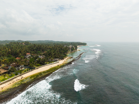 Aerial view of Thalpe Beach featuring the sandy shore turquoise ocean waves and lush palm tree forests in Talpe Southern Province Sri Lanka. Aerial view of Thalpe Beach featuring the sandy shore turquoise ocean waves and lush palm tree forests in Talpe Southern Province Sri Lanka.