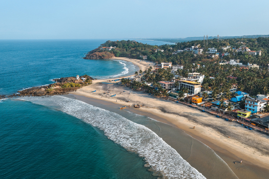 Aerial view of the crescent shaped sandy coastline with turquoise waves palm fringed hotels and rocky headlands under a clear blue sky in Kovalam Kerala India. Aerial view of the crescent shaped sandy coastline with turquoise waves palm fringed hotels and rocky headlands under a clear blue sky in Kovalam Kerala India.