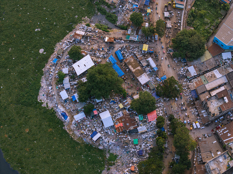 Aerial view of the Buriganga River bank featuring makeshift structures with blue tarps and green water hyacinth in Keraniganj Dhaka Division Bangladesh. Aerial view of the Buriganga River bank featuring makeshift structures with blue tarps and green water hyacinth in Keraniganj Dhaka Division Bangladesh.