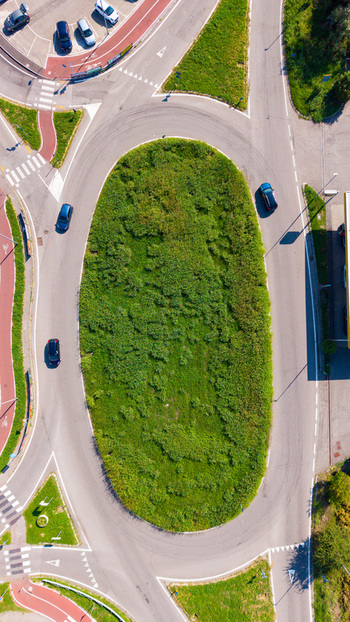 Aerial view of a traffic roundabout with a central grassy island surrounded by asphalt roads and moving cars in Mediglia Lombardy Italy. Aerial view of a traffic roundabout with a central grassy island surrounded by asphalt roads and moving cars in Mediglia Lombardy Italy.