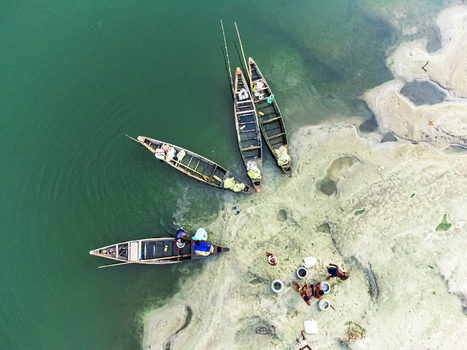 Khansama Upazila Bangladesh 12 September 2023 Aerial view of wooden boats moored on a sandy riverbank with people working near the green water.