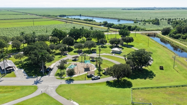 Aerial view of Pahokee Park featuring a playground picnic shelters and lush green trees surrounded by expansive agricultural fields and a canal in Pahokee Florida United States.