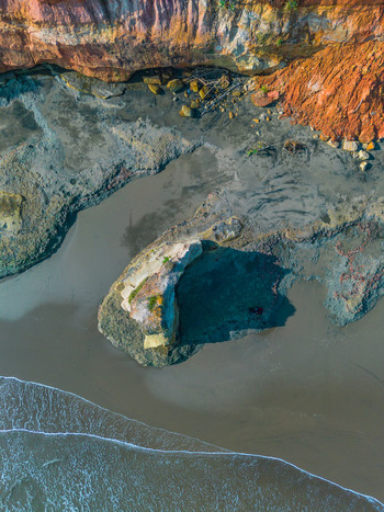 Aerial view of a rocky outcrop on a sandy beach with dramatic cliffs and ocean waves in Bali Bali Indonesia. Aerial view of a rocky outcrop on a sandy beach with dramatic cliffs and ocean waves in Bali Bali Indonesia.