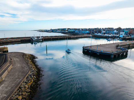 Aerial view of Bangor Harbour and Town with a sailboat navigating calm waters stone piers and coastal buildings in Bangor Northern Ireland United Kingdom.