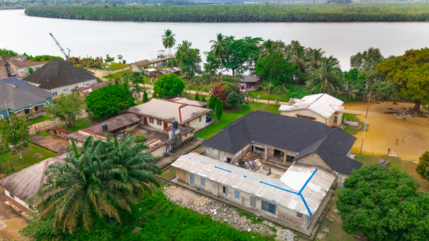 Aerial view of residential buildings and lush vegetation along the riverbank with a small pier in Minima Rivers Nigeria.