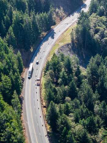 Aerial view of road construction on a winding highway through a dense evergreen forest with traffic cones and work vehicles in Gold Beach Oregon United States. Aerial view of road construction on a winding highway through a dense evergreen forest with traffic cones and work vehicles in Gold Beach Oregon United States.