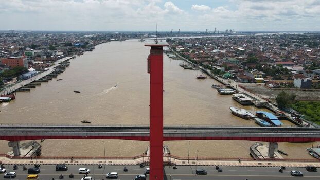 Aerial view of the red Ampera Bridge spanning the Musi River with urban development boats on the water and traffic in Kecamatan Seberang Ulu I Sumatera Selatan Indonesia. Aerial view of the red Ampera Bridge spanning the Musi River with urban development boats on the water and traffic in Kecamatan Seberang Ulu I Sumatera Selatan Indonesia.