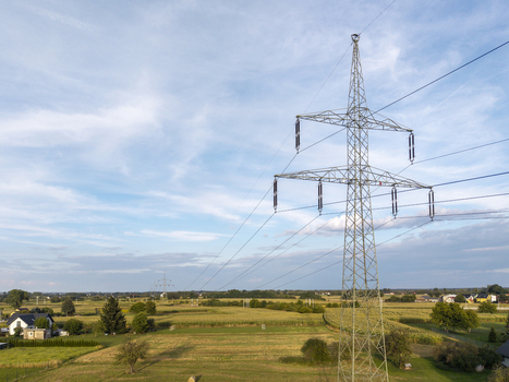 Aerial view of an electric pylon standing in a rural landscape with agricultural fields scattered houses and a clear blue sky in Poland. Aerial view of an electric pylon standing in a rural landscape with agricultural fields scattered houses and a clear blue sky in Poland.
