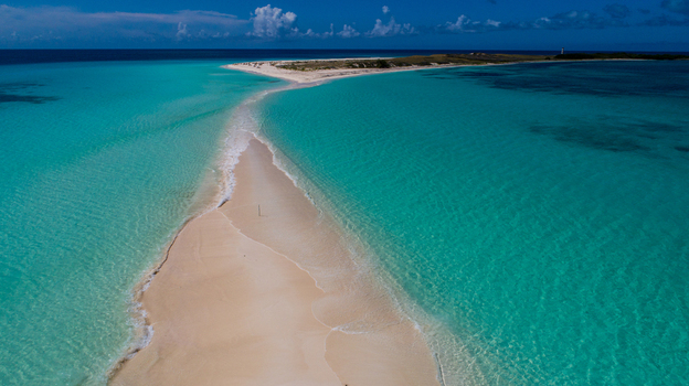 Aerial view of the Los Roques archipelago featuring a narrow sandbar extending into crystal clear turquoise water under a bright blue sky in Los Roques Dependencias Federales Venezuela. Aerial view of the Los Roques archipelago featuring a narrow sandbar extending into crystal clear turquoise water under a bright blue sky in Los Roques Dependencias Federales Venezuela.