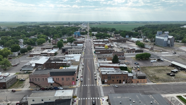 Aerial view of the main street cutting through buildings grain elevators and tree lines under a cloudy sky Wausa Nebraska United States.