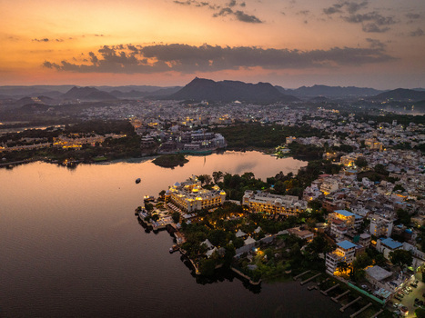 Aerial view of the Taj Lake Palace situated in Lake Pichola during a golden sunset with the city skyline and Aravalli hills in the background in Udaipur Rajasthan India.