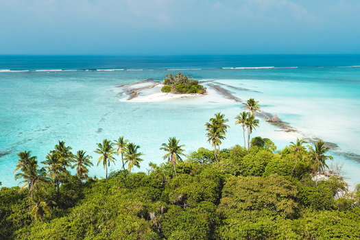 Aerial view of a lush tropical island with tall palm trees and dense vegetation surrounded by crystal clear turquoise lagoon water Innafinolhu Haa Alif Atoll Maldives. Aerial view of a lush tropical island with tall palm trees and dense vegetation surrounded by crystal clear turquoise lagoon water Innafinolhu Haa Alif Atoll Maldives.