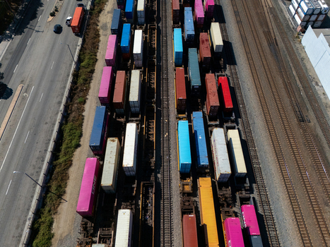 Aerial view of a freight train loaded with colorful shipping containers on parallel tracks next to a highway in Carson California United States.