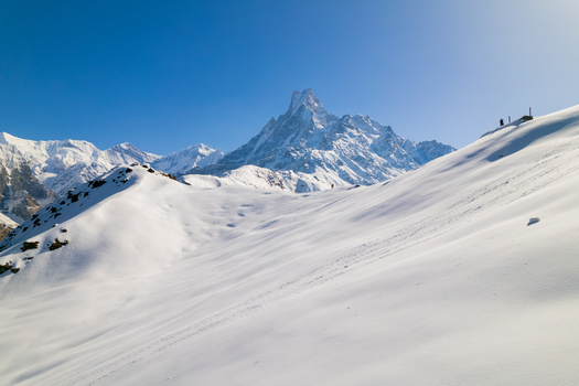 Aerial view of the snow covered peak of Machapuchare rising above the Himalayan landscape under a clear blue sky in Nepal.
