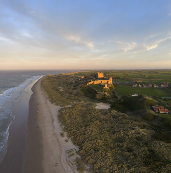 Aerial view of Bamburgh Castle overlooking the sandy beach and dunes at golden hour in Bamburgh England United Kingdom. Aerial view of Bamburgh Castle overlooking the sandy beach and dunes at golden hour in Bamburgh England United Kingdom.