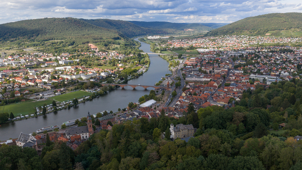 Aerial view of Mainbrucke spanning the Main river surrounded by historic red roofed buildings lush hills and winding riverbanks in Miltenberg Bayern Germany.