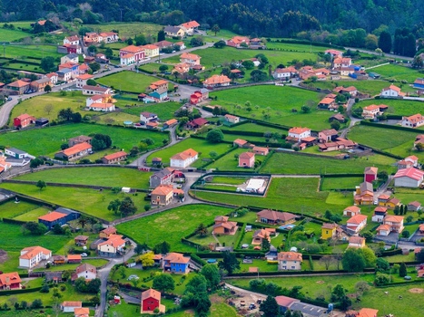 Aerial view of a rural village with red roofed houses nestled among green fields and lush vegetation in Cudillero Asturias Spain.