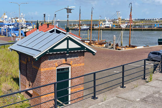 Den Oever Netherlands 20 May 2026 View of the historic former waterlevel gauge house at Vissershaven with fishing boats docked in the harbor under a clear blue sky. Den Oever Netherlands 20 May 2026 View of the historic former waterlevel gauge house at Vissershaven with fishing boats docked in the harbor under a clear blue sky.