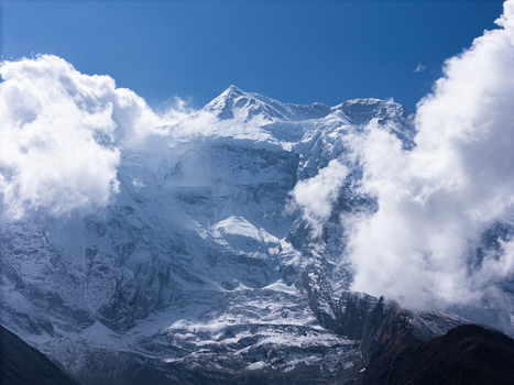 Aerial view of the snow covered peaks of the Himalayas with dramatic clouds and a clear blue sky in Nepal.