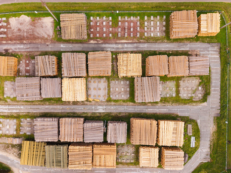 Aerial view of stacked lumber and timber piles arranged in an industrial yard with concrete foundations and surrounding grass in Brankas Jelgava Municipality Latvia. Aerial view of stacked lumber and timber piles arranged in an industrial yard with concrete foundations and surrounding grass in Brankas Jelgava Municipality Latvia.