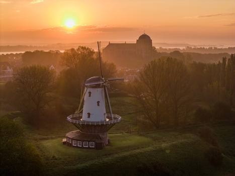 Aerial view of the historic De Koe windmill and the Grote Kerk church at sunset with misty fields and trees Veere Zeeland Netherlands.