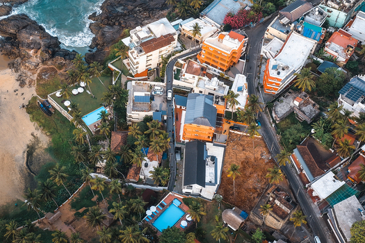 Aerial view of the coastal area near Vizhinjam featuring buildings swimming pools palm trees and the nearby beach in Kovalam Keralam India. Aerial view of the coastal area near Vizhinjam featuring buildings swimming pools palm trees and the nearby beach in Kovalam Keralam India.