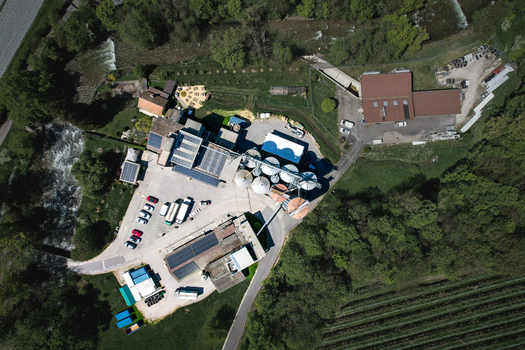 Aerial view of Moulin de la Vaux showing industrial silos solar panels on rooftops and a flowing river surrounded by lush green trees in Aubonne Vaud Switzerland. Aerial view of Moulin de la Vaux showing industrial silos solar panels on rooftops and a flowing river surrounded by lush green trees in Aubonne Vaud Switzerland.