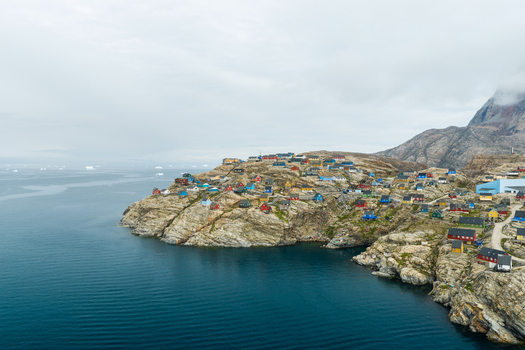 Aerial view of the colorful houses of Uummannaq village perched on the rocky coastline with icebergs floating in the calm sea in Uummannaq Kitaa Greenland. Aerial view of the colorful houses of Uummannaq village perched on the rocky coastline with icebergs floating in the calm sea in Uummannaq Kitaa Greenland.