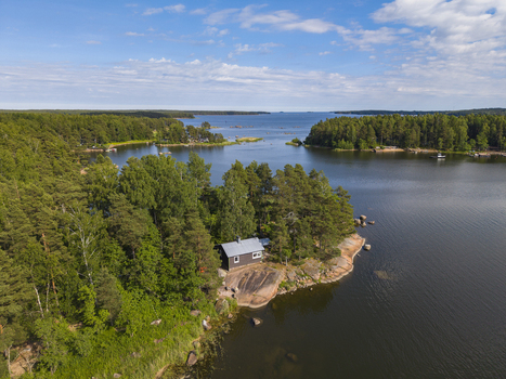 Aerial view of a small wooden cabin nestled on a rocky shoreline surrounded by dense pine forest overlooking a calm bay in Hamina Kymenlaakso Finland. Aerial view of a small wooden cabin nestled on a rocky shoreline surrounded by dense pine forest overlooking a calm bay in Hamina Kymenlaakso Finland.