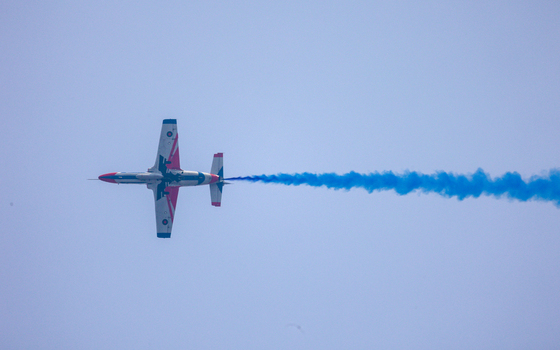 Dhaka Bangladesh 25 March 2026 View of a lone aircraft streaking across the sky leaving a vibrant trail of blue smoke against the pale expanse.