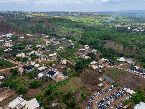 Aerial view of diverse homes winding dirt roads and a large full parking lot nestled within a vibrant green valley ohafia Abia Nigeria. Aerial view of diverse homes winding dirt roads and a large full parking lot nestled within a vibrant green valley ohafia Abia Nigeria.