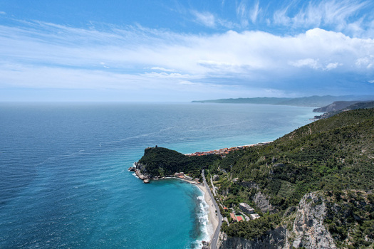 Aerial view of the Promontorio di Varigotti overlooking the turquoise sea sandy beach and lush green hills under a blue sky in Varigotti Liguria Italy. Aerial view of the Promontorio di Varigotti overlooking the turquoise sea sandy beach and lush green hills under a blue sky in Varigotti Liguria Italy.