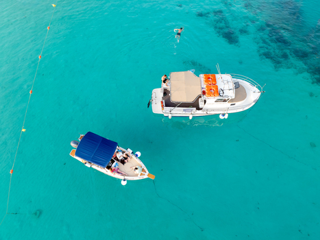Aerial view of white boats floating on crystal clear turquoise waters with a swimmer nearby creating a vibrant contrast of colors and textures Blue lagoon Comino Malta. Aerial view of white boats floating on crystal clear turquoise waters with a swimmer nearby creating a vibrant contrast of colors and textures Blue lagoon Comino Malta.