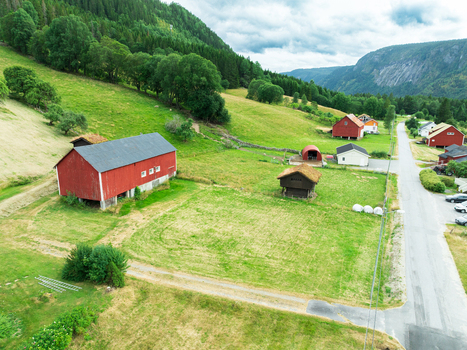 Aerial view of traditional red wooden barns and farm buildings nestled in a lush green valley with rolling hills and a road in Araksbo Agder Norway.