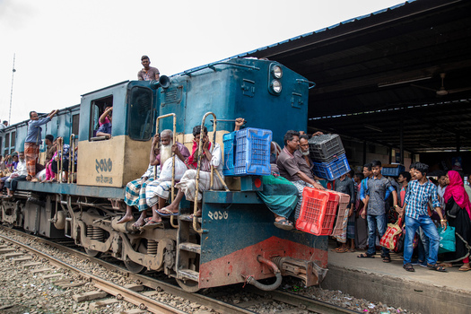 Dhaka Bangladesh 14 June 2018 View of Airport Railway Station with passengers sitting on the exterior of a blue locomotive and people on the platform with plastic crates. Dhaka Bangladesh 14 June 2018 View of Airport Railway Station with passengers sitting on the exterior of a blue locomotive and people on the platform with plastic crates.
