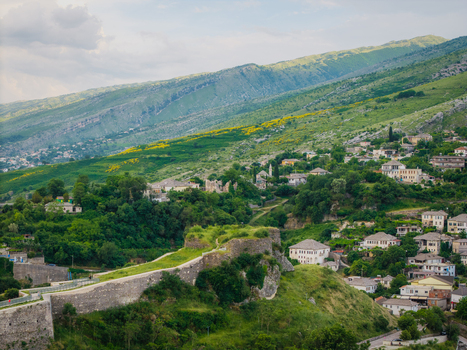 Aerial view of the historic stone walls of Gjirokaster Fortress overlooking traditional Ottoman houses and lush green hills in Gjirokaster Gjirokaster County Albania. Aerial view of the historic stone walls of Gjirokaster Fortress overlooking traditional Ottoman houses and lush green hills in Gjirokaster Gjirokaster County Albania.